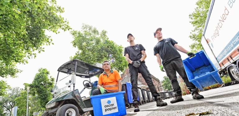 Vuilnismannen met een beperking staan met blauwe kratten op straat