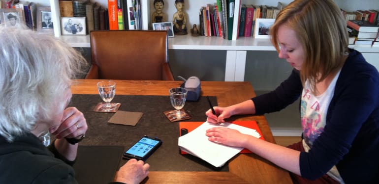 Sandra Suijkerbuijk zit aan een tafel met een oudere mevrouw om te praten over zorgtechnologie. 