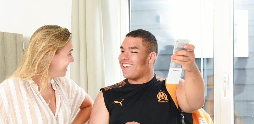 Begeleider en bewoner kijken elkaar aan, bewoner heeft een afstandsbediening vast 