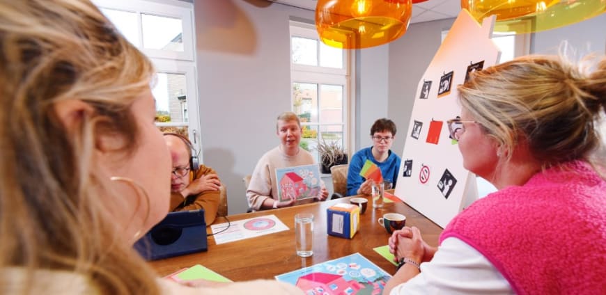 Een groep zorgprofessionals zit aan tafel en in gesprek met ervaringsdeskundigen tijdens een workshop.
