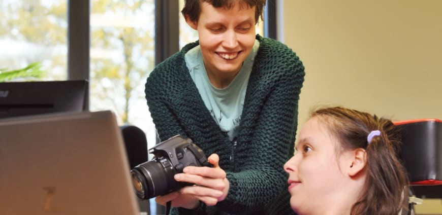 Fotograaf laat op de camera een foto zien aan een vrouw in een rolstoel.