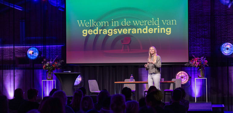 Foto van een inspiratiebijeenkomst, met op de presentatie de tekst: 'welkom in de wereld van gedragsverandering'.
