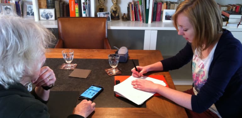 Sandra Suijkerbuijk zit aan een tafel met een oudere mevrouw om te praten over zorgtechnologie. 