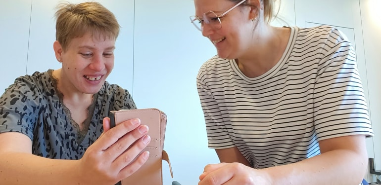 Cliënt en begeleider kijken samen lachend naar de telefoon