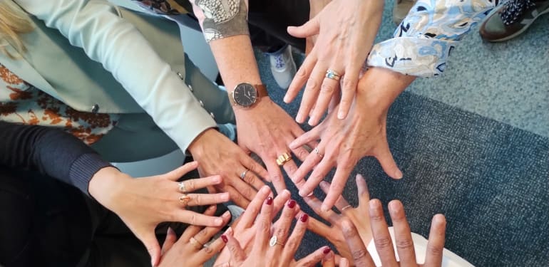 Groep mensen die hun handen samen in het midden leggen als symbool voor samenwerking en verbinding.