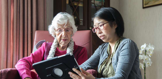 zorgverlener-met-aziatisch-uiterlijk-en-oude-dame-ipad-tablet